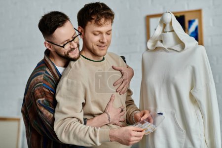 Téléchargez les photos : Un couple gay se tient côte à côte dans un atelier de designer, travaillant ensemble sur une tenue tendance. - en image libre de droit