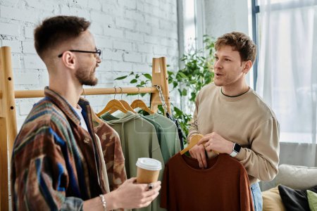 Téléchargez les photos : Deux hommes, un couple gay, se tiennent côte à côte dans un atelier de designer, créant passionnément des vêtements tendance. - en image libre de droit