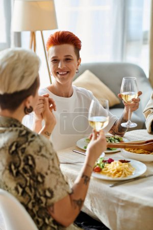 A sophisticated woman sits at a table, savoring a glass of wine, with friends.