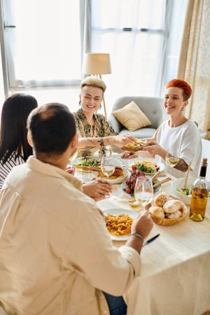 Vielfältige Gruppe, die sich eine Mahlzeit teilt, darunter ein liebevolles lesbisches Paar.