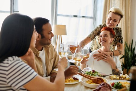 Foto de Una pareja lésbica cariñosa organiza una cena con diversos amigos en casa, rodeada de calidez y compañía. - Imagen libre de derechos