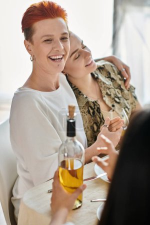 Dos mujeres saboreando una botella de vino en una mesa, con amigos.