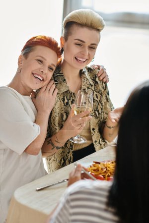 Foto de Two women standing by a table, part of a diverse group enjoying a meal. - Imagen libre de derechos