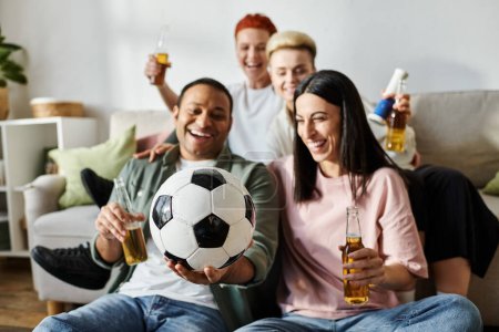 Diverse group of friends sitting on couch, holding beers and a soccer ball.