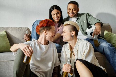 Diverse group of friends and loving lesbian couple sitting together on a couch at home.