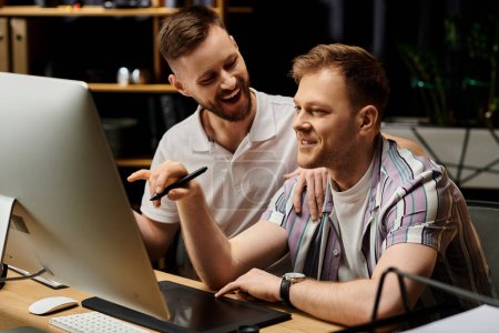 Zwei glückliche, stilvoll gekleidete Männer, die in einem modernen Büro zusammenarbeiten und sich auf einen Computerbildschirm konzentrieren.