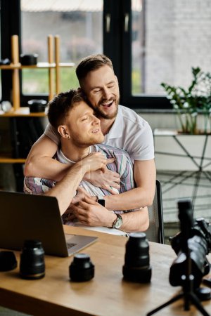 Téléchargez les photos : Deux hommes en tenue décontractée partageant une étreinte chaleureuse tout en travaillant devant un ordinateur portable. - en image libre de droit