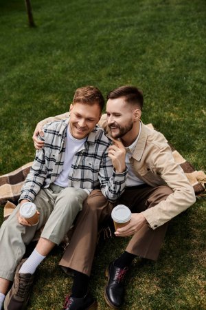 Two men in casual attire enjoy a peaceful moment on a blanket in the grass.