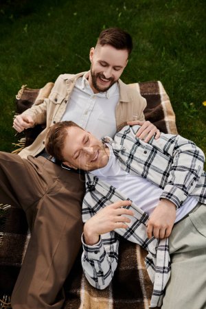 Zwei Männer in lässigen Outfits liegen draußen auf einer Decke.