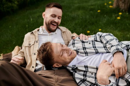 Couple of men in casual attire relaxing on grassy field.
