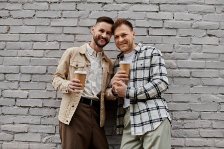 Happy gay couple in casual attire enjoying drinks outdoors.