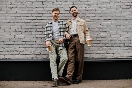 Two men in comfortable attire standing in front of a brick wall.
