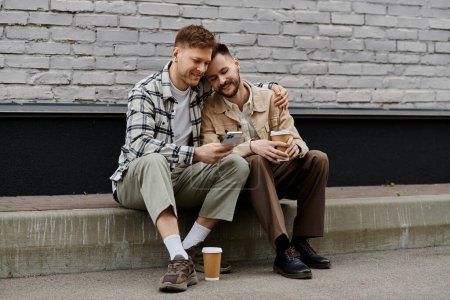 Deux jeunes hommes en tenue décontractée assis, absorbés dans un téléphone portable.