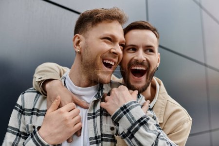 Two men smiling and hugging outdoors in comfy attire.