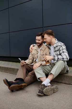 Zwei Männer in Freizeitkleidung sitzen auf dem Boden, in ihre Handys vertieft.