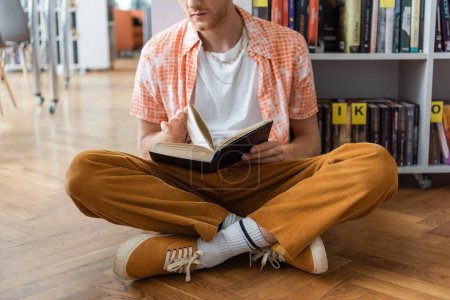 Young man absorbed in reading while seated on floor.