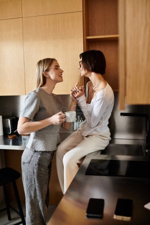 Téléchargez les photos : Deux jeunes femmes partagent un moment confortable dans une cuisine d'hôtel, savourant leur café ensemble. - en image libre de droit