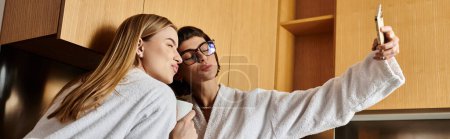 Junges lesbisches Paar in Bademänteln hat Spaß, als Frau ein Selfie mit Mann macht.