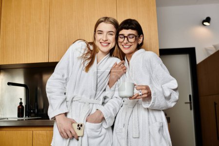 Two women, a young lesbian couple, wearing bath robes, standing next to each other in a hotel room.