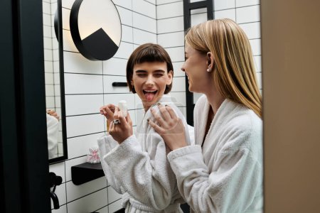 A young woman in a bathrobe flossing her teeth in front of a mirror in a hotel bathroom.