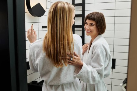 Foto de Una mujer está de pie frente a un espejo dentro de un baño de hotel, con una bata de baño. - Imagen libre de derechos
