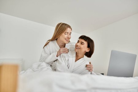 Téléchargez les photos : Un jeune couple lesbien en peignoir couché au lit, partageant un moment tendre de connexion et de détente. - en image libre de droit