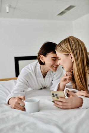 Téléchargez les photos : Deux femmes en peignoirs de bain reposent paisiblement côte à côte sur un lit d'hôtel luxueux, partageant un moment tendre de proximité et de connexion. - en image libre de droit