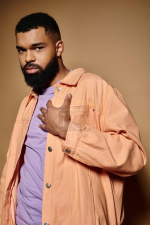 Schöner afroamerikanischer Mann mit Bart und orangefarbener Jacke posiert vor einer lebendigen Kulisse.
