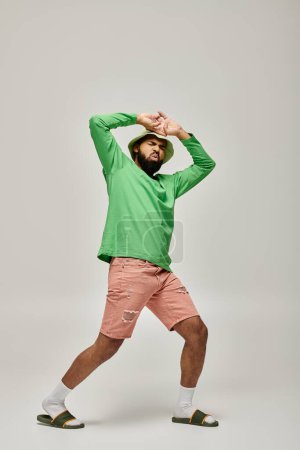 Handsome African American man posing in fashionable green shirt and pink shorts against vibrant backdrop.