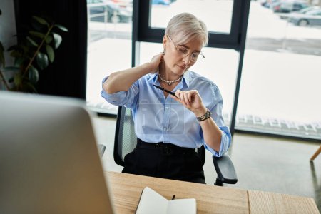 Una mujer de negocios de pelo corto de mediana edad trabaja diligentemente en el escritorio de su oficina durante la menopausia..