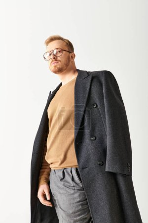 Handsome man in stylish long coat and glasses posing confidently.