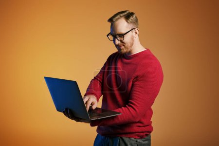 Stilvoller Mann im roten Pullover, der aktiv einen Laptop benutzt.