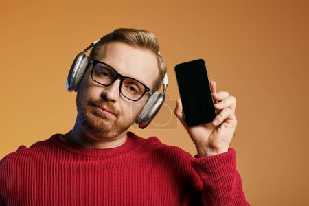 A stylish man listening to music on headphones while holding a cell phone.