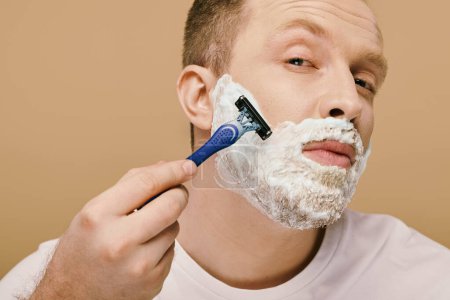 A man in casual attire carefully shaves his face with a razor.