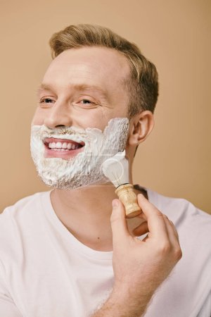 A handsome man in casual attire applying shaving cream with a brush.