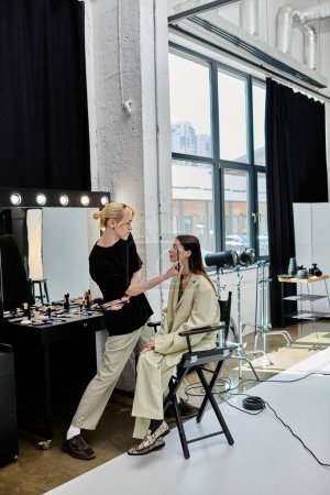 Woman sits in chair, facing mirror, next to stylist.