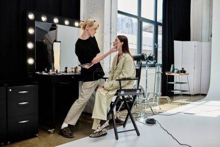 A woman sits in a chair, as a skilled makeup artist works on her face in front of a mirror.