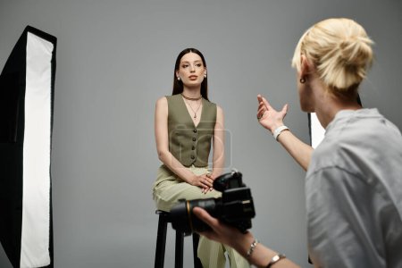 A woman elegantly sits on a stool in front of a photograph.