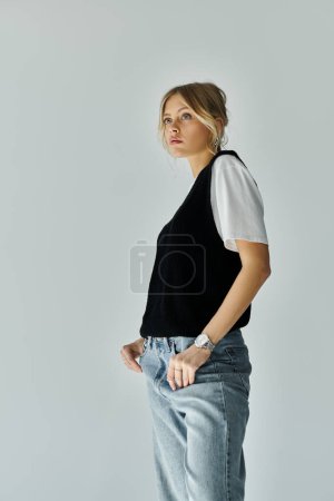 Stylish young blonde woman standing confidently with hands in pockets on a grey background.