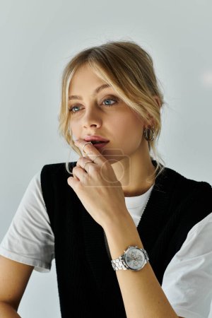 A chic, young woman with blonde hair is elegantly sporting a stylish watch on her wrist against a grey backdrop.