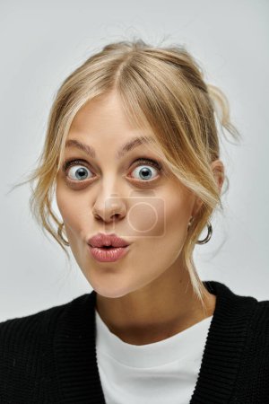 A stylish young woman with blonde hair wearing casual attire looks surprised.