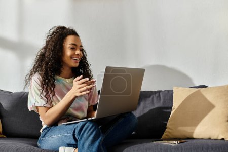Woman sitting on couch, working on laptop.