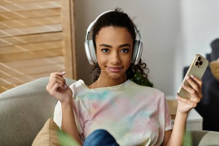 Woman on couch, wearing headphones, with cellphone.