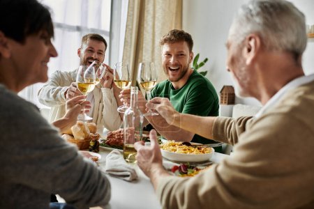 Photo for A gay couple toasts with parents during a joyous dinner gathering. - Royalty Free Image