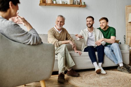 A gay couple sits on a couch with parents, smiling and talking.