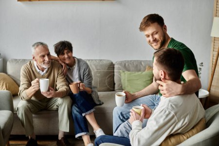 Ein schwules Paar sitzt auf einem Sofa, umarmt und hält Tassen, im Hintergrund die Eltern.
