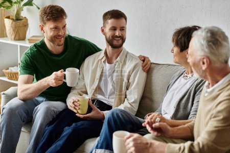 A gay couple sits with parents on a couch in a living room, enjoying a conversation and cups of coffee.
