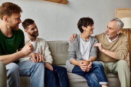 A gay couple sits with parents on a couch, engaging in a warm and intimate conversation.