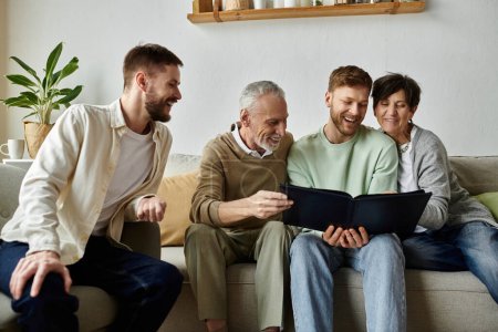 A gay couple laughs with parents while looking at an old photo album together on the couch.