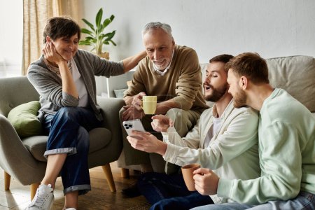 A gay couple sits on a couch with parents in their home, sharing news or viewing something on a phone.